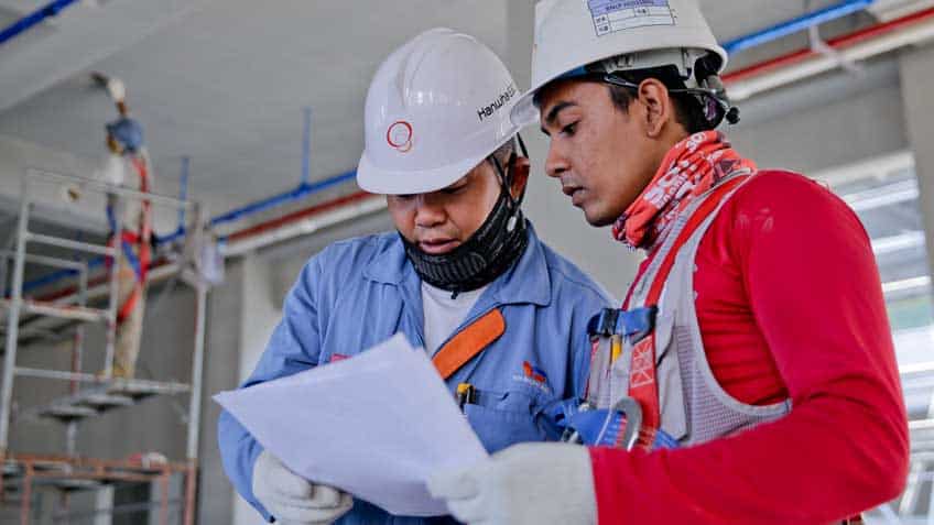 Two men wearing construction gear looking at notes
