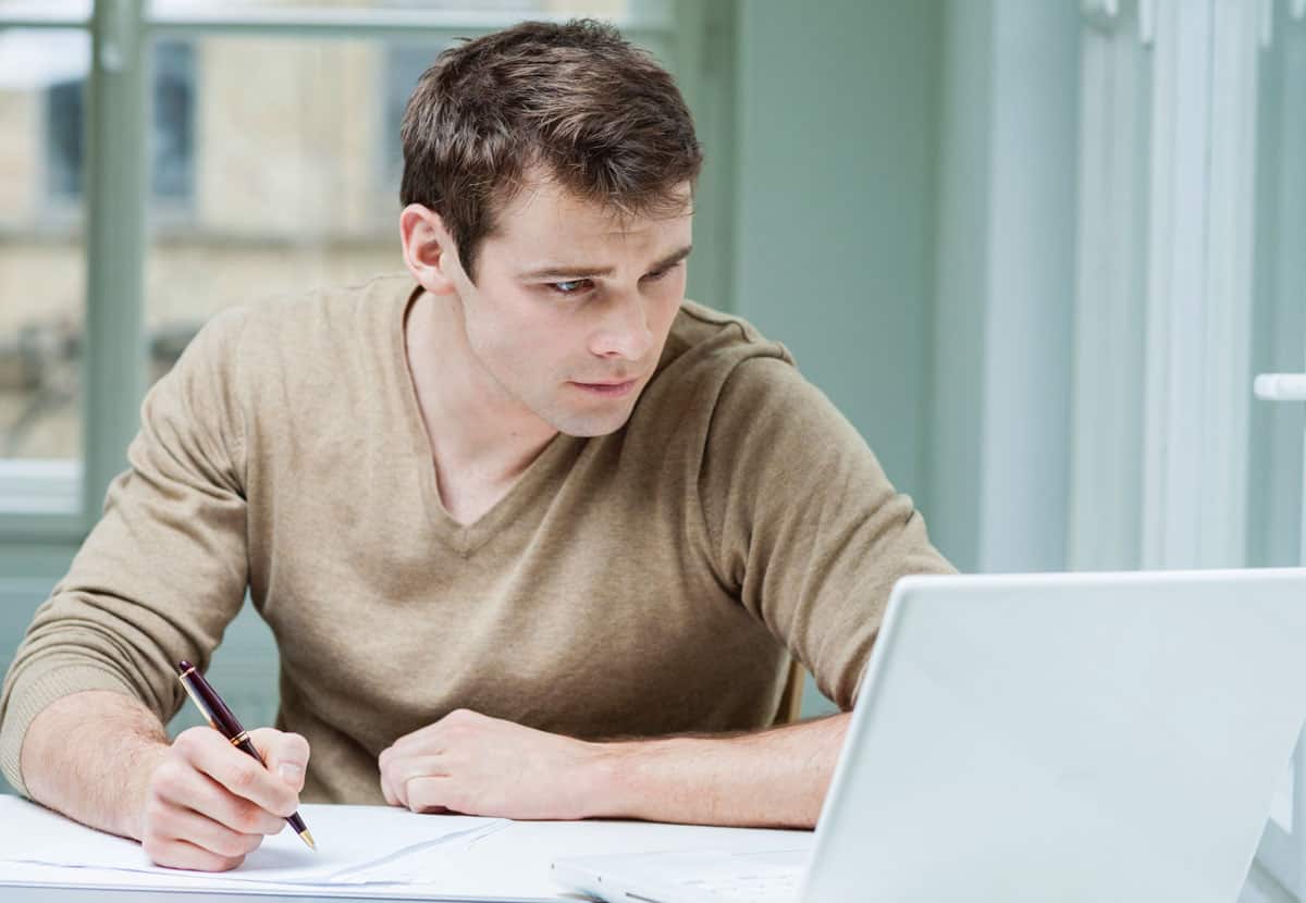 College student looking at laptop while writing notes