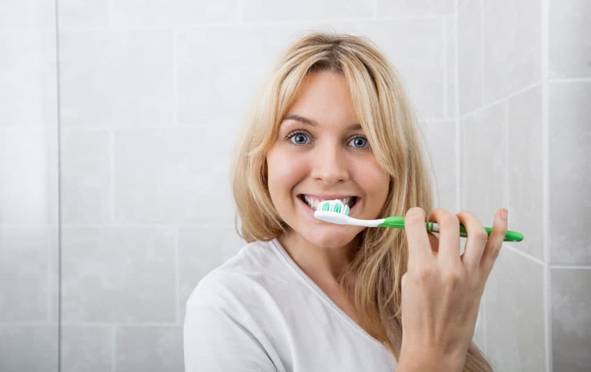 Young woman brushing teeth in bathroom.